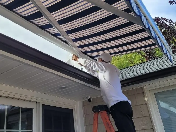 A Rollup Awnings installer fitting a retractable awning to a home on Long Island